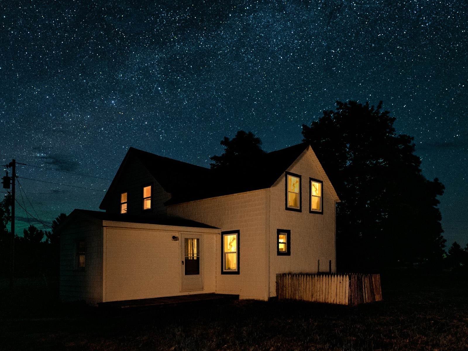 Farmhouse glowing with warm interior and porch light under a starry night sky